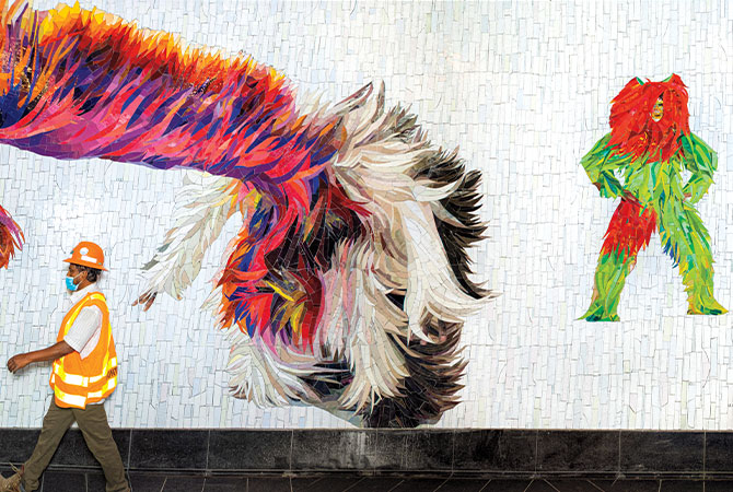 Enlargeable photo of subway worker walking past mosaic characters on subway wall