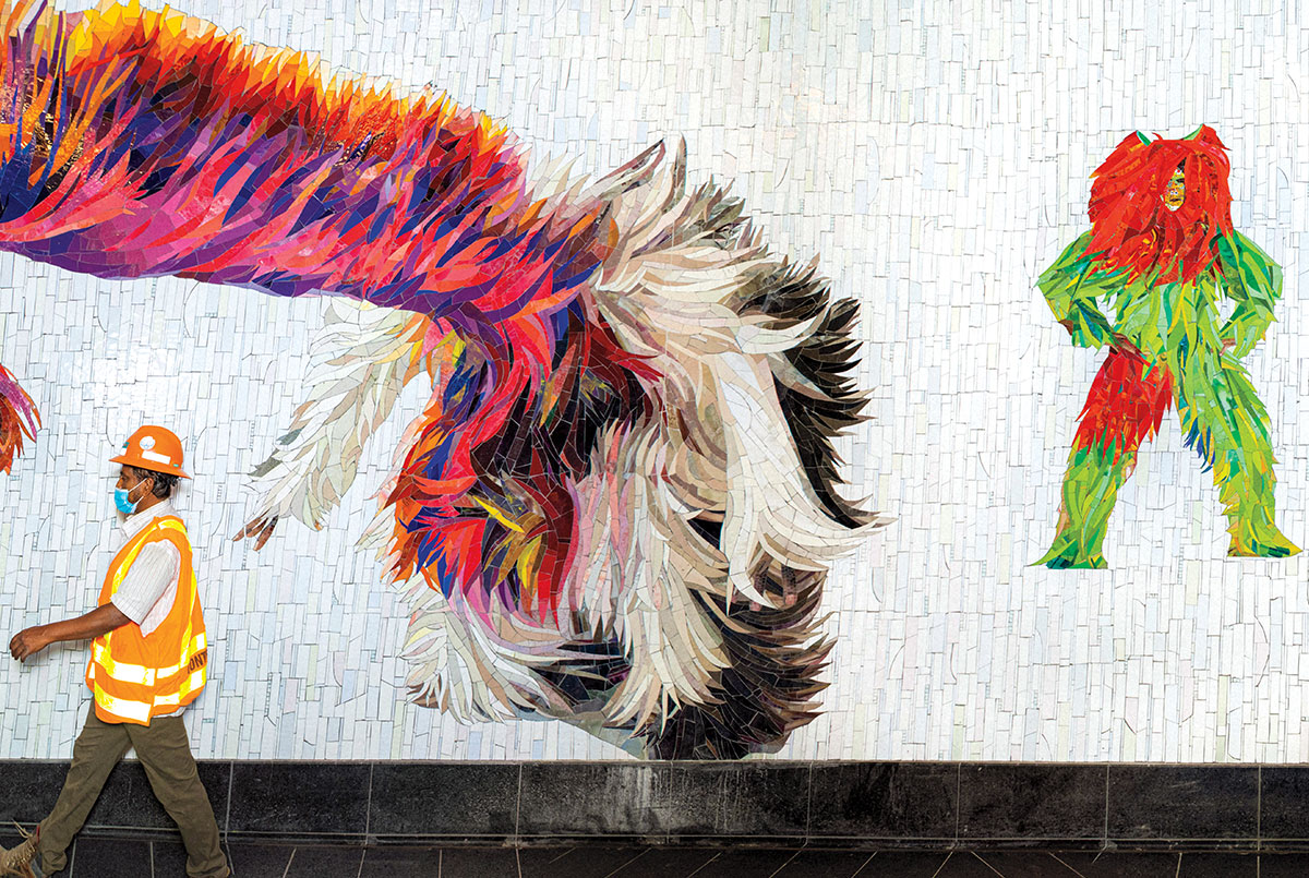 Subway worker walking past mosaic characters on subway wall