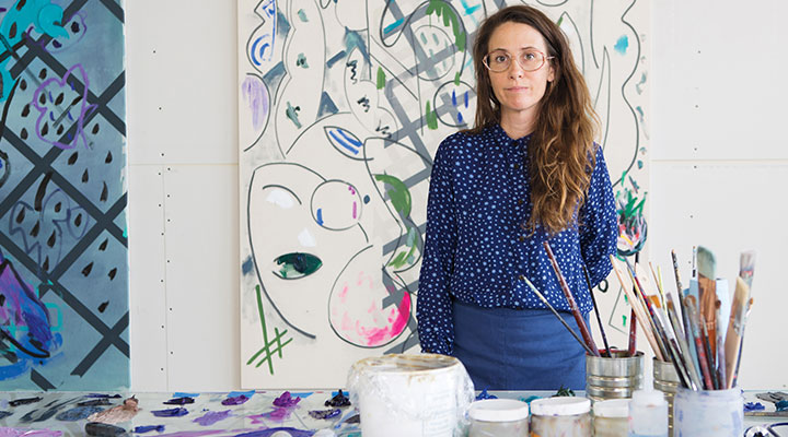 Person wearing all blue standing in front of an abstract painting