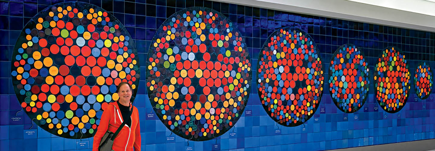 Image of an artist standing in front of one of their pieces which is mosaic circles